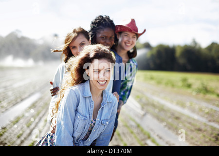 Quattro giovani donne in un campo pieno di piantine un organico raccolto con sprinkler la spruzzatura di acqua in background Foto Stock