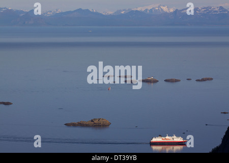 Grande nave passeggeri passando da minuscole isolette rocciose nei pressi di isole Lofoten con montuoso costa norvegese in background Foto Stock