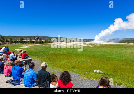 I turisti a guardare Eruzione del geyser Old Faithful con Old Faithful Inn in background, il Parco Nazionale di Yellowstone, Wyoming USA Foto Stock