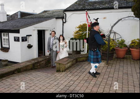 Gli sposi a piedi dal vecchio fabbro del negozio in Gretna Green, Scozia, preceduto da un piper Foto Stock