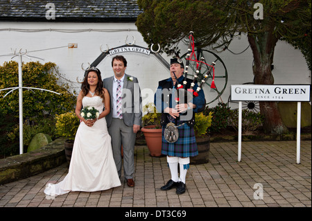 Gli sposi pongono al di fuori del Vecchio fabbro del negozio in Gretna Green, Scozia, accompagnato da un piper Foto Stock