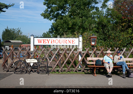 Giovane seduto accanto alla stazione segno e vecchia bicicletta alla stazione di Weybourne sulla North Norfolk Railway Foto Stock