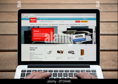 Il sito web di Argos su un MacBook contro una panca in legno sfondo all'aperto tra cui un uomo le dita (solo uso editoriale). Foto Stock