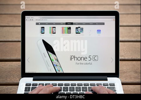 Apple iPhone del sito web su un MacBook contro una panca in legno sfondo all'aperto tra cui un uomo le dita (solo uso editoriale). Foto Stock