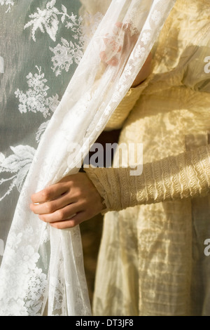 Una giovane donna indossa e vintage Edwardian vestito come lei pone di fronte a una tendina di pizzo. Foto Stock