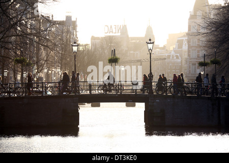 Silhouette di persone e biciclette a cavallo su un ponte su un canale ad Amsterdam, Olanda Foto Stock