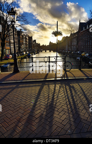 Silhouette di una bicicletta parcheggiata e la sua ombra su un ponte su un canale al tramonto in Amsterdam, Olanda Foto Stock