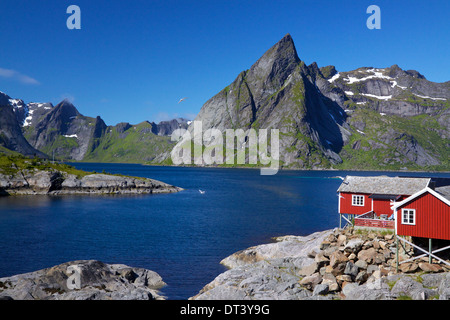 Scenic fjord sulle isole Lofoten con rosso tipico rifugio di pesca e imponenti picchi di montagna Foto Stock