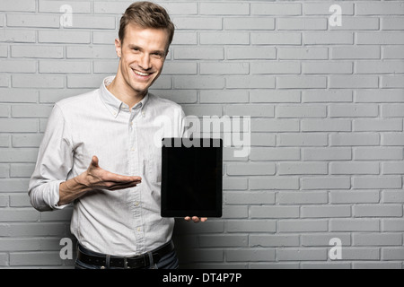 Ritratto di modello maschile presentando tablet in studio con sfondo grigio, guardando la fotocamera Foto Stock