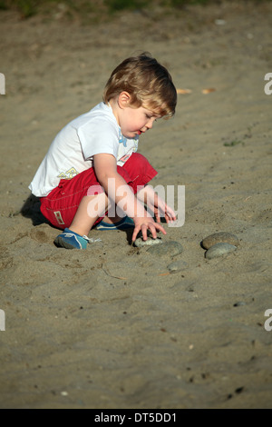 Piccolo ragazzo giocando con pietre su una spiaggia Foto Stock