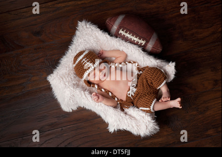 A 12 giorni di età neonato Bambino addormentato in una pelliccia cassa e indossare una maglia di football americano in costume. Foto Stock