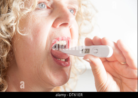 Donna prendendo la propria temperatura usando un termometro digitale Foto Stock