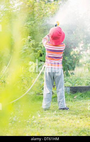 Stile di vita estate scena. Bambina di irrigazione di piante da giardino e verdure con sprinkler. Foto Stock