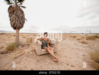 Giovane donna rilassante in poltrona nel deserto Foto Stock