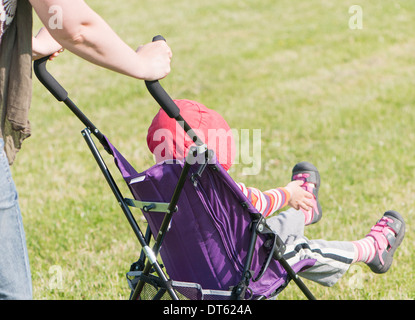 Madre passeggiate nel parco con la figlia in passeggino Foto Stock