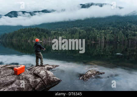 L'uomo pesca dalle rocce, Lago Buntzen, British Columbia, Canada Foto Stock