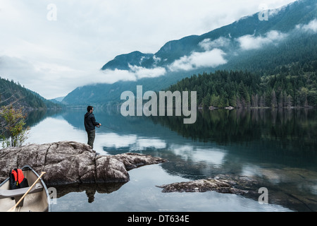 L'uomo pesca dalle rocce, Lago Buntzen, British Columbia, Canada Foto Stock