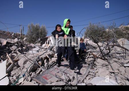 Un uomo palestinese sta con i suoi figli sulle macerie della sua casa dopo che esso è stato demolito dal comune israeliano escavatrice che le autorità credono senza autorizzazione comunale nel quartiere di 'Wade avvento' della città di Silwan a Gerusalemme il 10 febbraio 2014. Israele concede raramente palestinesi permette di costruire in Cisgiordania, compresa Gerusalemme Est. Esso ha demolito almeno 27.000 abitazioni palestinesi e le strutture in quanto occupa la West Bank nel 1967, secondo il Comitato israeliano contro le demolizioni di case. Foto di Saeed Qaq Foto Stock