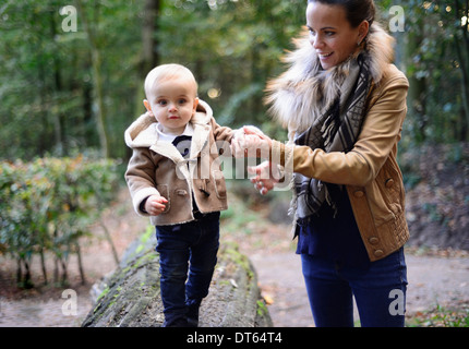 La madre a piedi toddler maschio sul tronco di albero Foto Stock