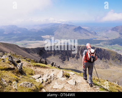 Escursionista che porta uno zaino camminando giù Rhyd Ddu sul percorso principale di Bwlch con vista verso sud per Llechog da Mt Snowdon Mountain in Snowdonia (Eryri), Wales, Regno Unito Foto Stock