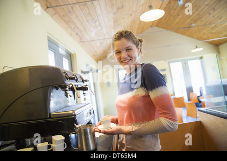 Una giovane donna che fa il caffè utilizzando una grande macchina da caffè. Foto Stock