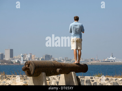 Un uomo equilibrato su un cannone sulla Ile de Goree guardando verso la terraferma Dakar, Senegal Foto Stock