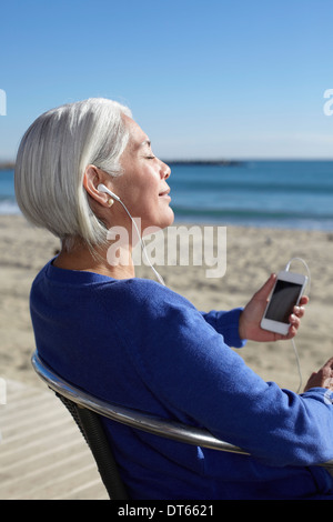 Donna matura l'ascolto di musica con cuffie auricolari sulla spiaggia