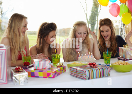 Ragazza adolescente che spegne le candeline sulla torta del compleanno con gli amici Foto Stock