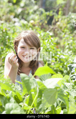 Una giovane ragazza seduta in tra i freschi Fogliame verde di un giardino. Ortaggi e fiori. Il prelievo di verdure fresche. Foto Stock