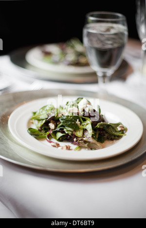 Una formale messa in tavola per un pasto. Cina piatti e bicchieri. Un organico di insalata mista con foglie. Foto Stock