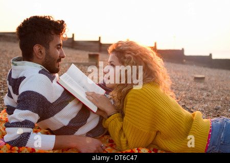 Coppia giovane sdraiato sulla spiaggia, donna libro di lettura Foto Stock