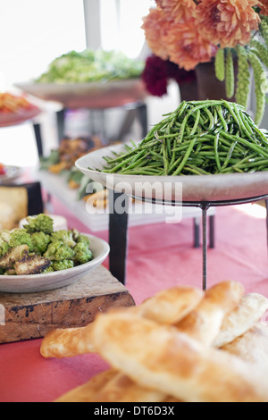 Insalate e verdure e frutta su piatti, stabilite per una festa. Una tabella di carico. Fiori in un vaso. Una fattoria stand stallo alimentare. Foto Stock