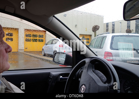 Uomo anziano in attesa in auto in coda davanti al gate del MOT testing centre per un motore annuale ispezione del veicolo Foto Stock