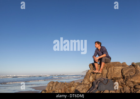 Uomo seduto sulla roccia in riva al mare a Foto Stock