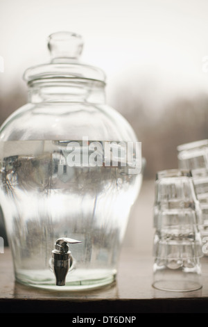 Acqua potabile in una grande e chiaro contenitore in vetro. Una pila di bicchieri. Pura acqua refrigerata. Foto Stock