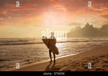 Giovane uomo che porta le tavole da surf sulla spiaggia di Ipanema, Rio de Janeiro, Brasile Foto Stock