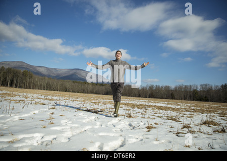 Un uomo in un cavo ponticello in maglia e muck stivali in piedi con le braccia distese, in un innevato paesaggio rurale. Foto Stock