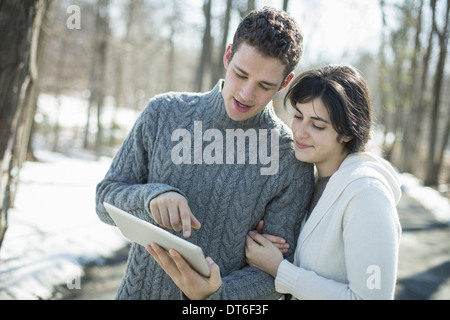 Una coppia in cerca di un computer tablet. In piedi vicino insieme su una giornata invernale nel bosco. Foto Stock