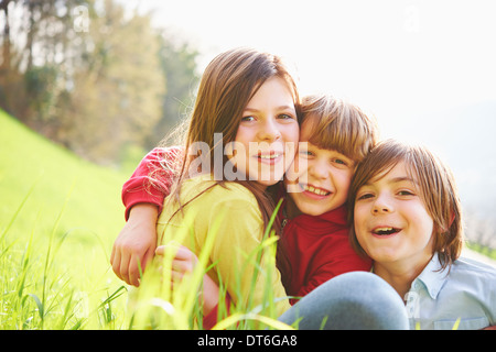 Sorelle e fratelli più giovani seduti in campo erboso Foto Stock