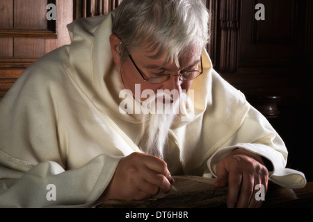Monaco con barba grigia iscritto in un libro antico Foto Stock