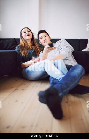 Bel giovane azienda telecomando cambiando canali seduto con la sua bella ragazza ridere mentre si guarda la TV. Foto Stock