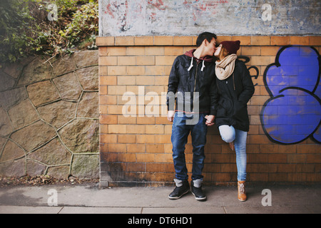 Affettuosa giovane adolescente kissing all'aperto contro un muro su strada. Razza mista matura nell'amore. Foto Stock