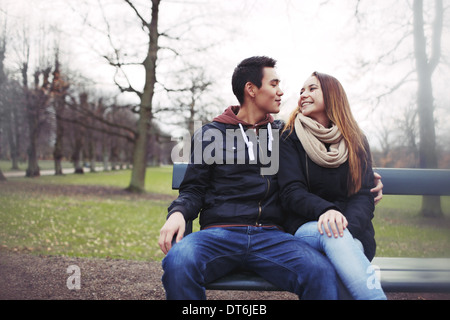 Felice coppia giovane seduta su una panchina all'aperto durante la stagione invernale. Asian teenage matura in vestiti caldi seduti su una panchina nel parco. Foto Stock