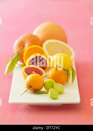 Un piatto bianco con arance arance pigmentate, pompelmi, limoni e limette su un tessuto rosa sfondo. Foto Stock