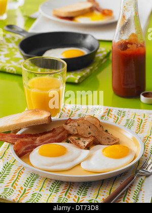 Una scena di prima colazione con il lato soleggiato di uova fritte, pancetta, toast, prima colazione patate e un bicchiere di succo di arancia Foto Stock