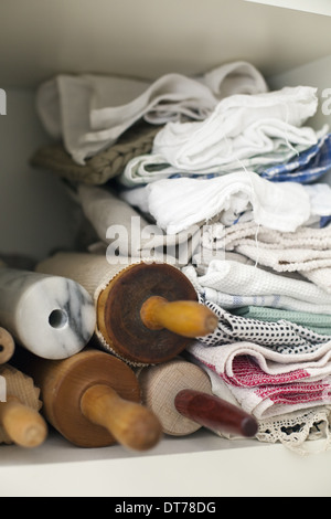 Un ripiano impilati con panni, biancheria da letto e una piccola pila di perni di rotolamento o fusi in legno. Foto Stock