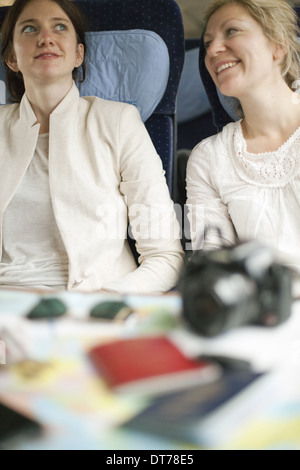 Due donne seduti su un treno, fianco a fianco. Fotocamera, passaporti e gli occhiali da sole sul tavolo di fronte a loro. Foto Stock