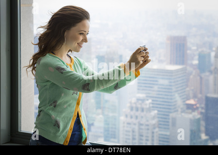 Uno stile di vita urbano. Una giovane donna con la sua fotocamera per scattare una foto da un osservatorio sui tetti della città. Foto Stock