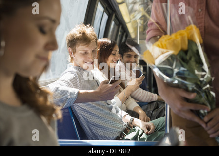 Uno stile di vita urbano. Un gruppo di persone, di uomini e di donne su un autobus cittadino, nella città di New York. Due persone che controllano i loro smart phone. Foto Stock