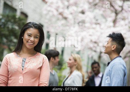 La vita della città in primavera. I giovani all'aperto in un parco della città. Una donna in maglia rosa con quattro persone in background. Foto Stock